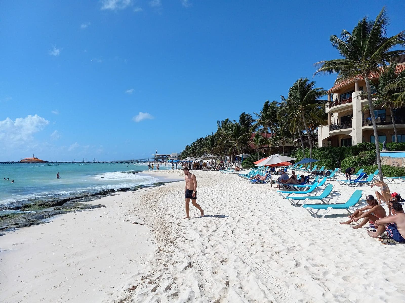 Plage de sable blanc à Playa del Carmen, avec des chaises longues et des palmiers au bord de l’eau