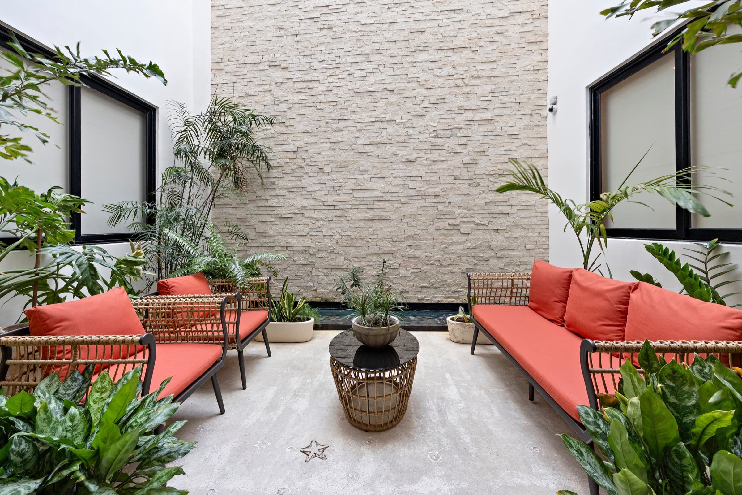 Jardín interno de Mare Condo: sala al aire libre con sillones coral, mesa de centro y plantas